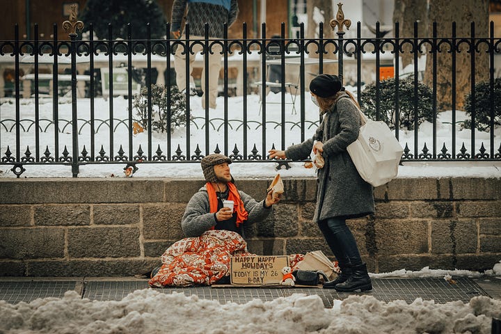 A homeless person is receiving something from the lady