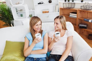 Two cute women drinking coffee together on a sofa at home