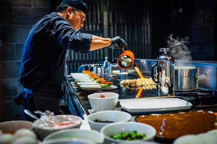 A chef skillfully applies a blowtorch to flambe codfish in a restaurant kitchen.