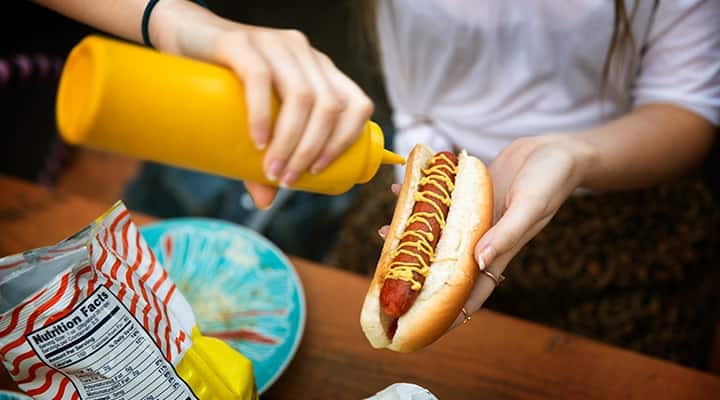 Woman putting mustard onto a hot dog that contains nitrates