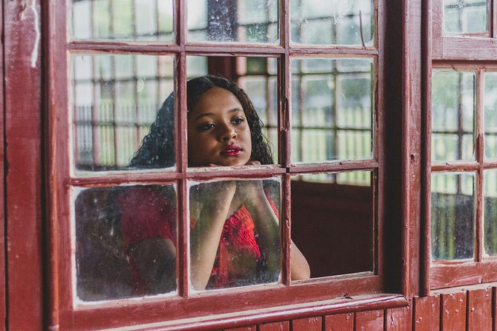 An ethnic woman wistfully looking through a window with missing glass panes