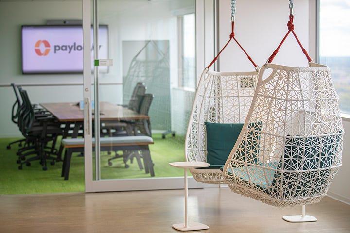 Two hanging chairs in a modern office setting with Paylocity logo in the background