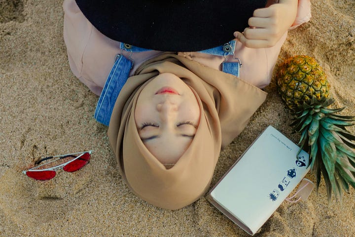 Woman wearing a hijab, lying on the sand beside her sunglasses