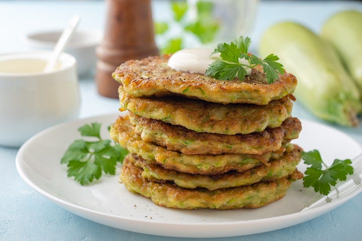 Zucchini fritters with fresh parsley and sour cream on a plate on a blue concrete background.