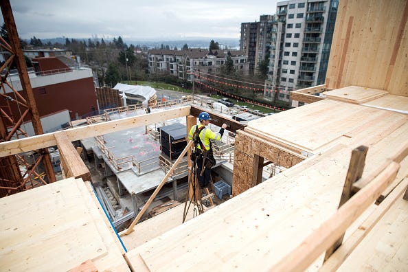 Photograph of a construction worker working on a timber building. In the background there are houses and high-rises.