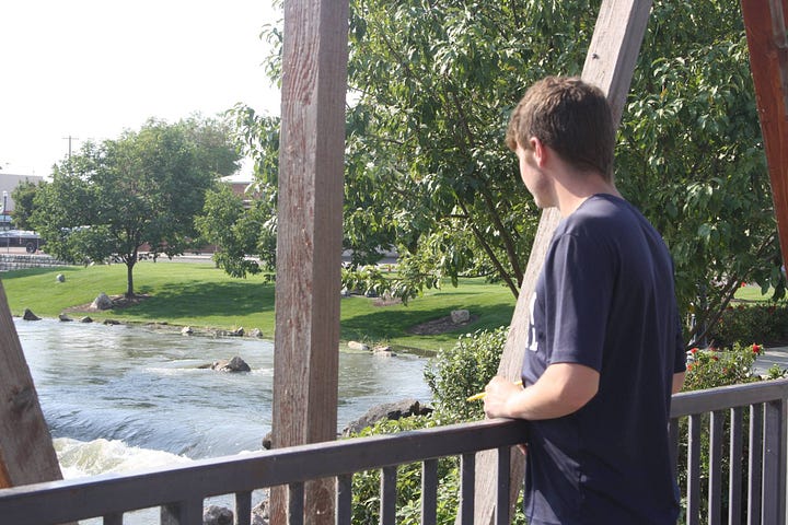 Teenage boy standing on a bridge looking at a river.