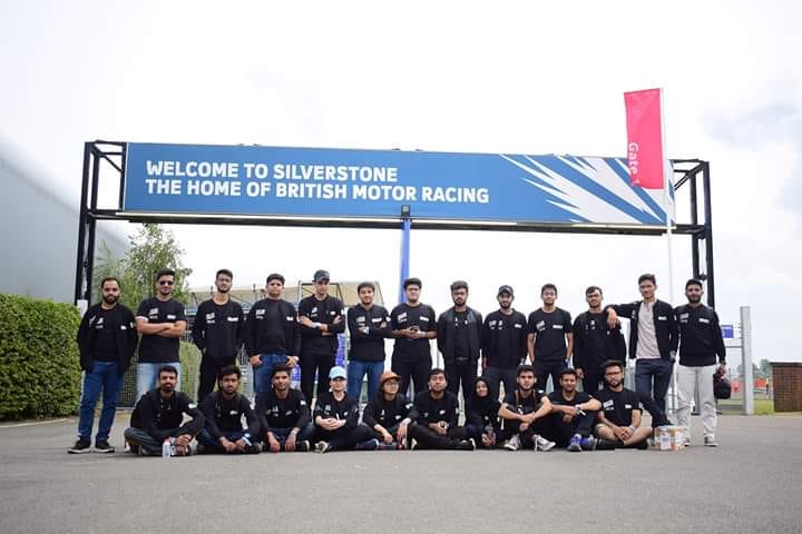 A team of students standing beneath a billboard welcoming them to a Formula Student competition