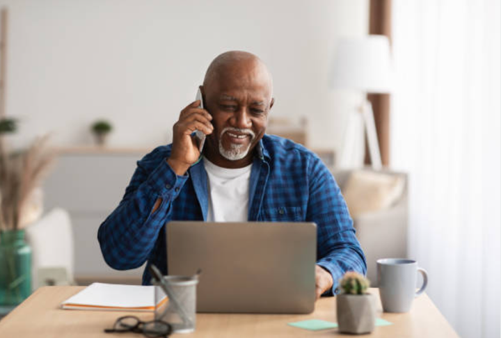 Older man talking on phone while on laptop.