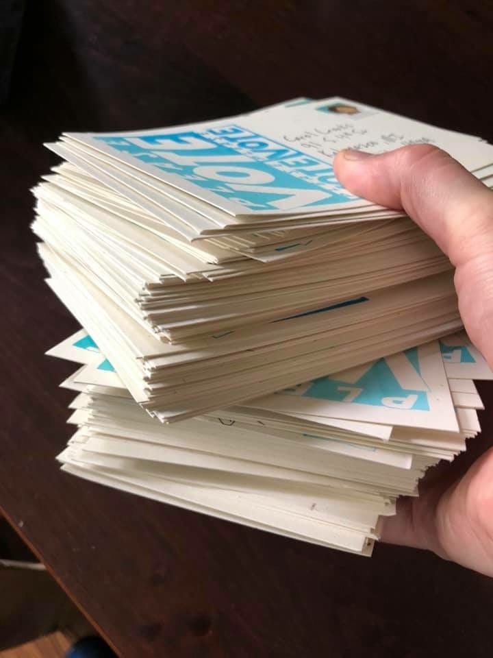 A hand holding a stack of postcards that read Please Vote