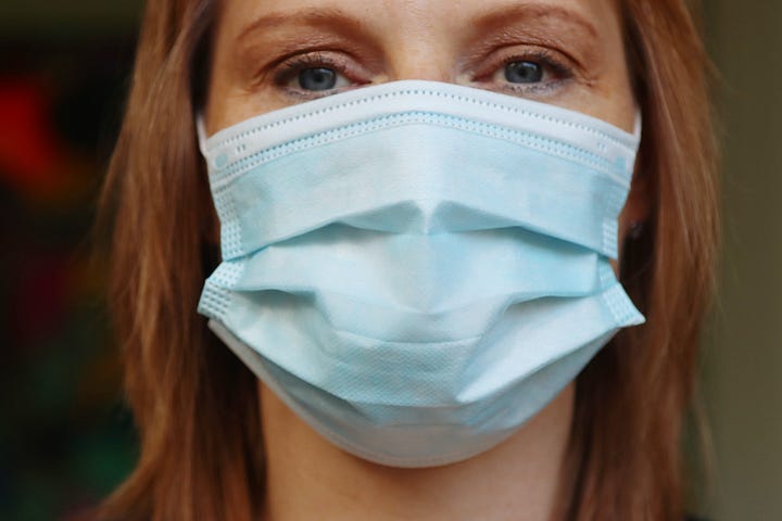 A woman with red hair and green eyes wearing a blue surgical mask