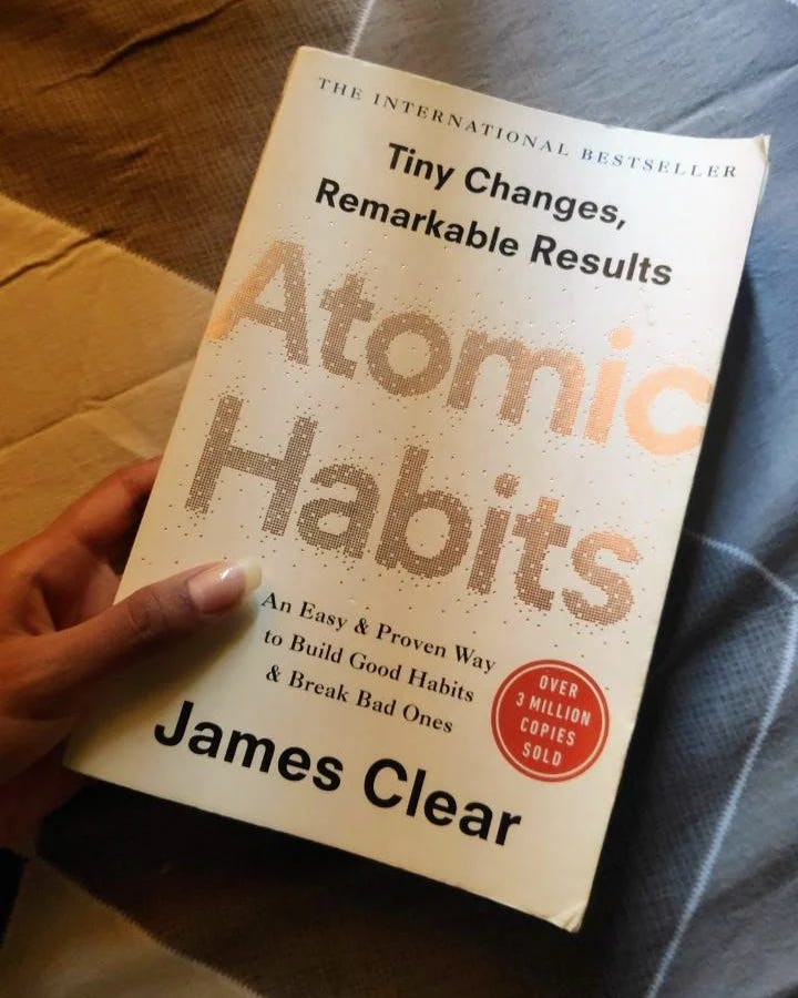 The book Atomic Habits by James Clear held in one hand over a slight grey background.