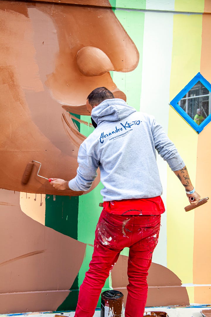 Alexandre Keto applying paint on to his mural with his back turned to the camera.