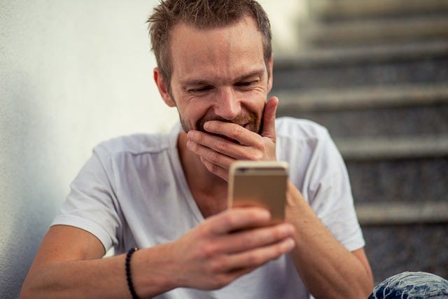 A man covering his mouth with his hand while looking at his phone