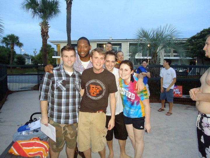 Curtis and a group of others are smiling at the camera on a beach in front of some palm trees.