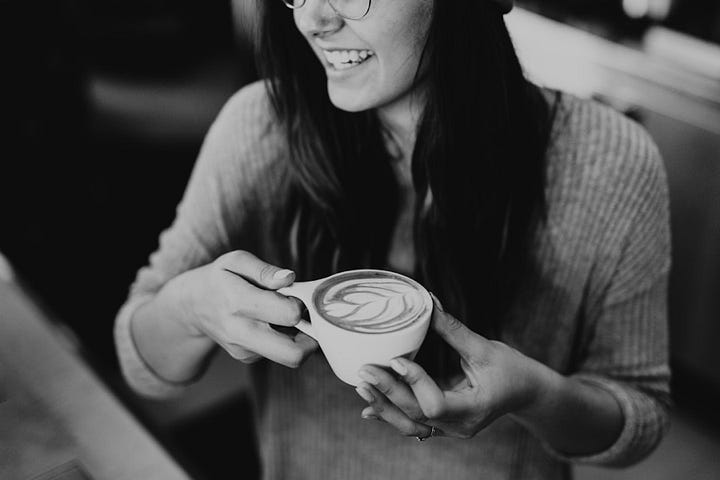 Brooke Cagle took this photo of a smiling woman holding a cappuccino in both hands.