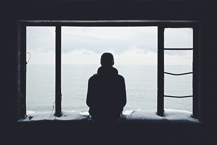 A solitary figure, seen in silhouette, sits on an open windowsill.