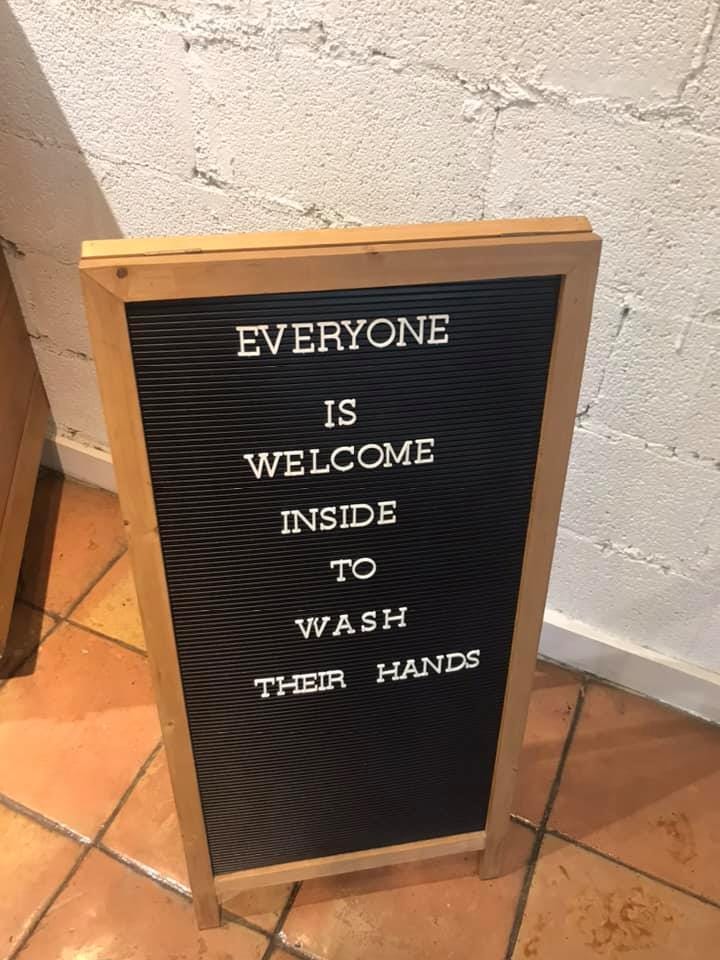 A shop sign stating that everyone is welcome to come in and wash their hands.