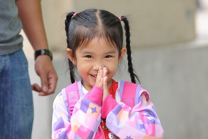 Young Asian girl smiling with her hands together in front of he mouth