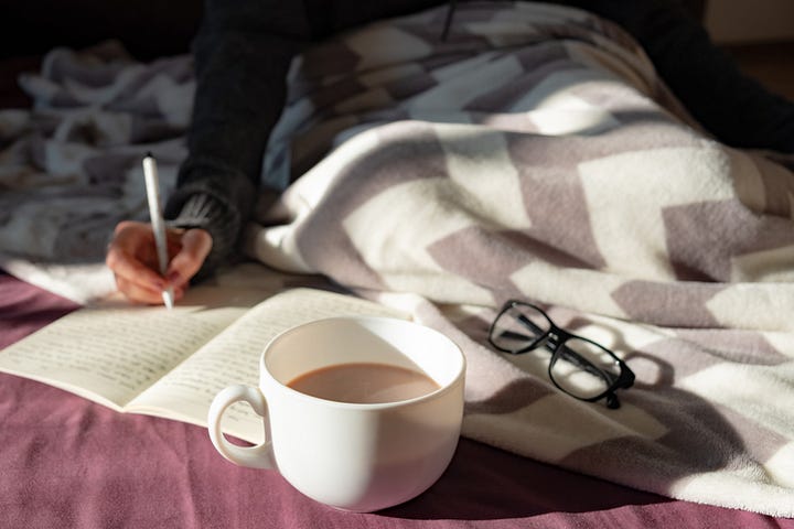 A person writing and having coffee in bed