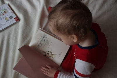Photo of baby from above opening a book while sitting on a blanket/