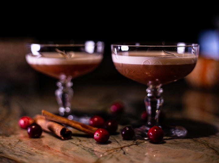 Autumn Whiskey Bitter in coupe, with cranberries and cinnamon on the table