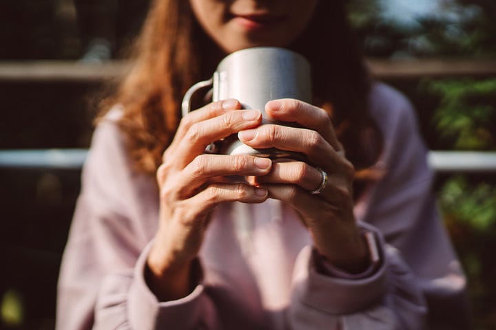 Close-up of a lady’s hands holding a coffee cup outdoors