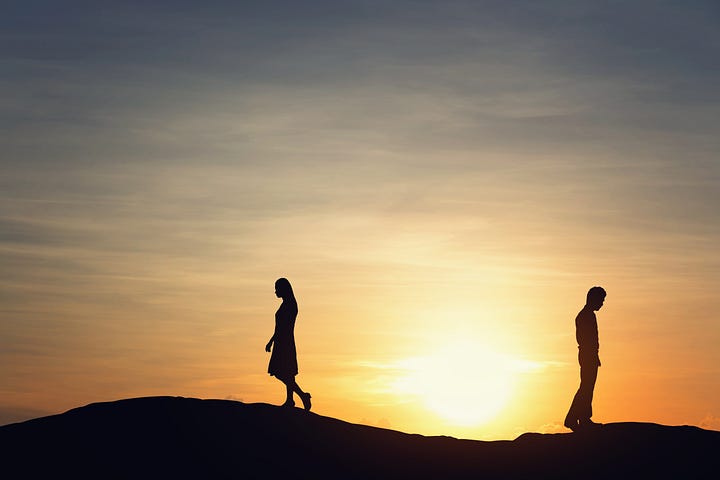 Silhouettes of a man and a woman walk away from each other in front of a sunset.