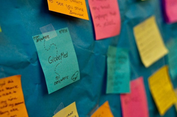 Colorful post-it notes, on which are written reflections about GlobeMed, are taped to a dark blue paper background.