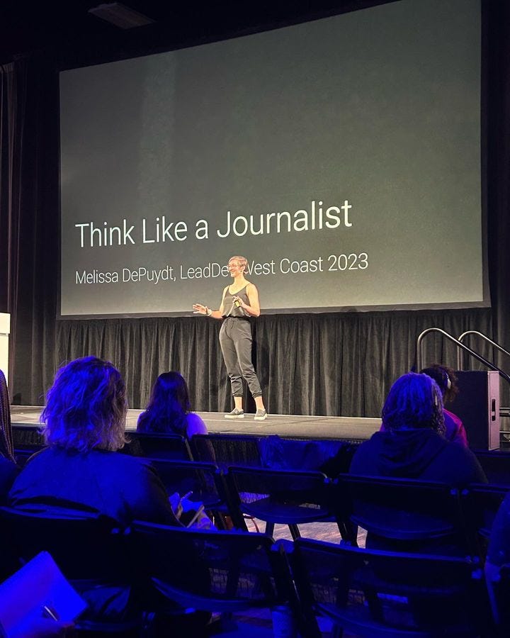 The author giving a talk on stage at an engineering leadership conference in 2023. The title slide behind her says, “Think like a journalist”