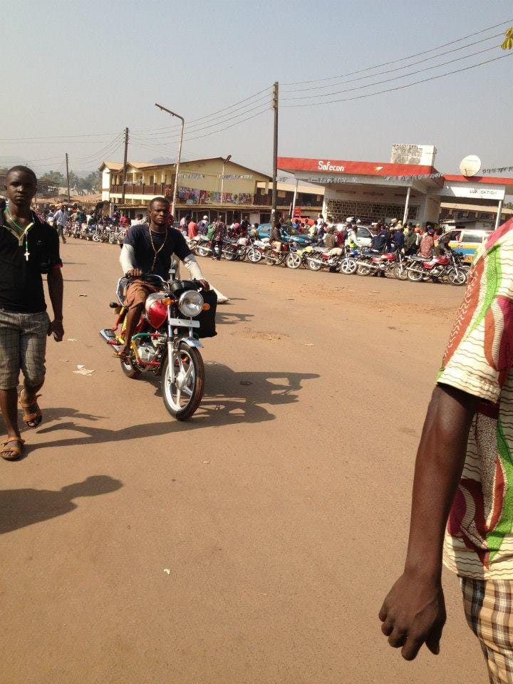 Motorbike riders standing next to their bikes awaiting passengers at the City Center in Makeni, Sierra Leone.