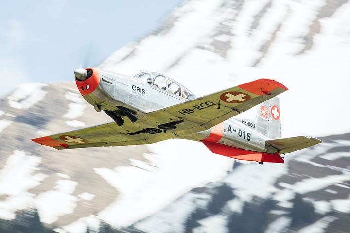 On point publishing’s chosen pic of a silver swiss sports plane flying across a mountain scene viewed from front and below with swiss flags on the place