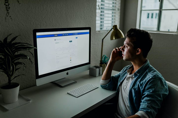 Person sitting at a desk, looking at a computer screen showing a social media site.