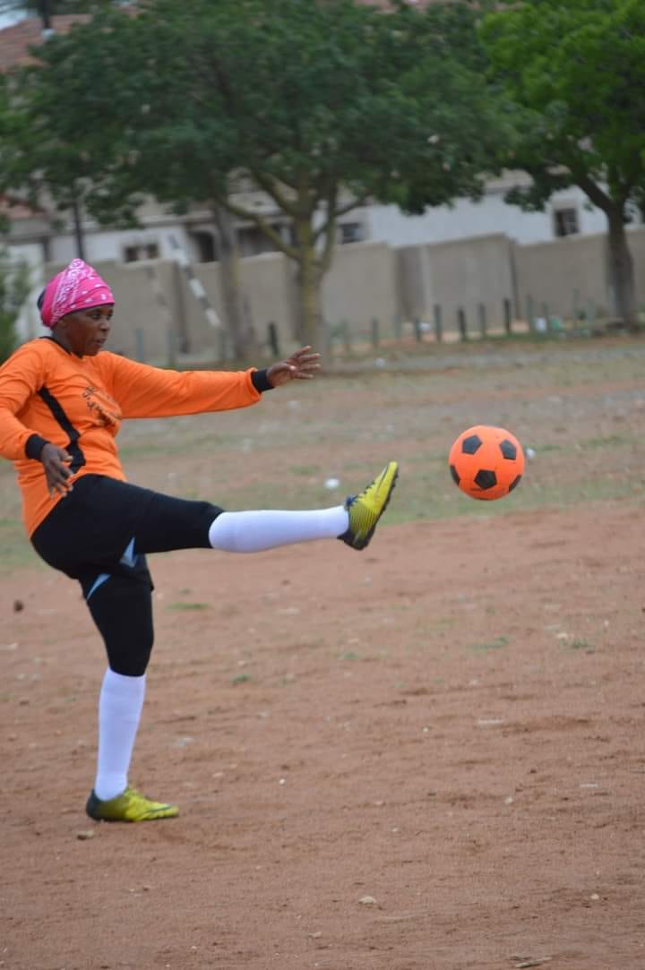 A woman in an orange shirt kicking an orange soccer (football) ball.
