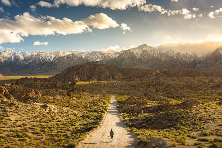 A solitary person walks along a desert path toward mountains.
