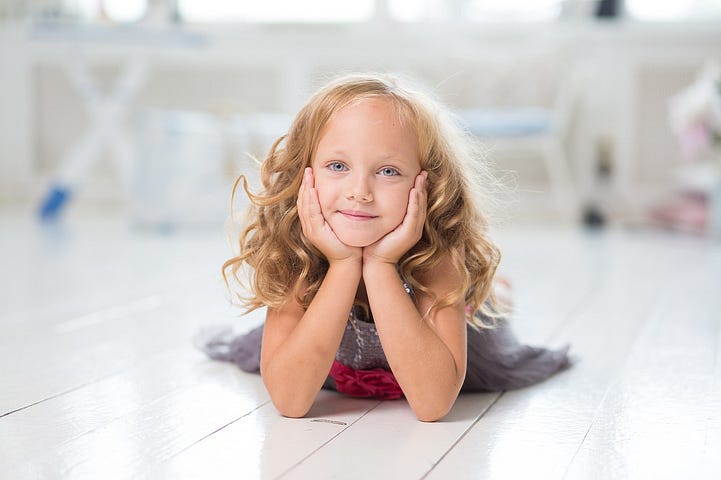 Little girl, lying on the floor, head in hands, a wistful look on her face.