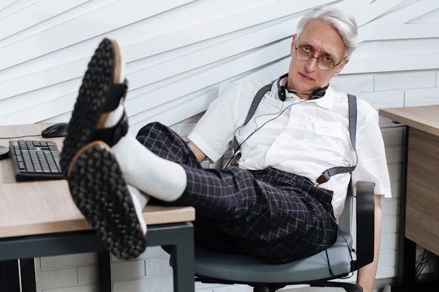 An elderly man sitting in his office chair with his legs on the desk