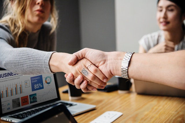 White women at the business table shaking hands.