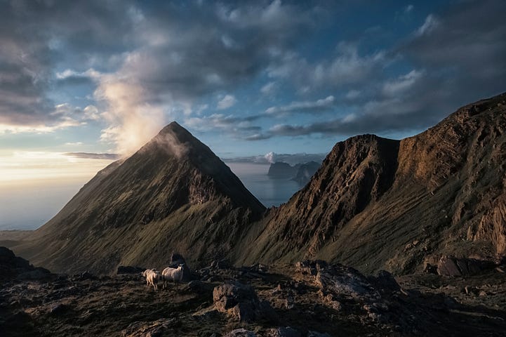 People Sitting on Brown Rock Mountain Under White Clouds