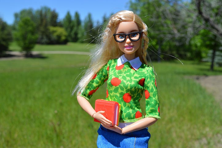 Barbie doll with blonde hair and glasses holding red books.
