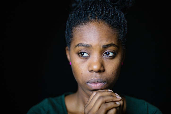 A woman in a green top looking worried and depressed. Solid black background.