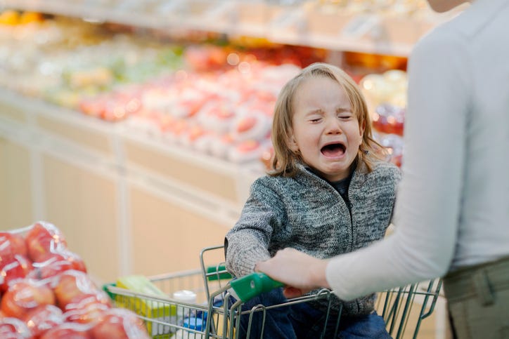 Toddler sitting in grocery cart crying in produce aisle