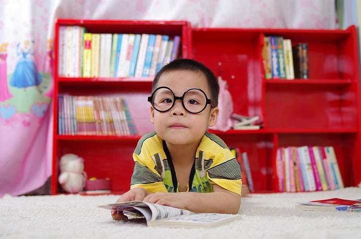 A boy with large round glasses pages through a paper book