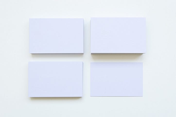 Four Stacks Of Plain Sized White Business Cards Against A White Background.