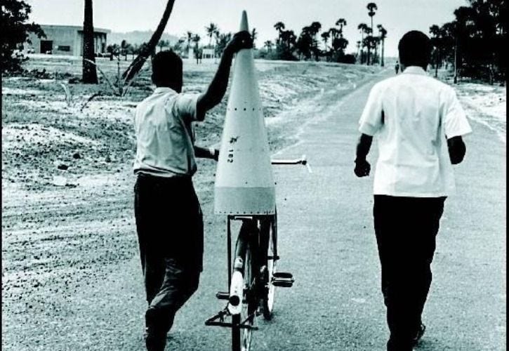 Picture of two men carrying Nike Apache rocket (first by India) equipment on a bicycle for assembly, two hours before the launch.