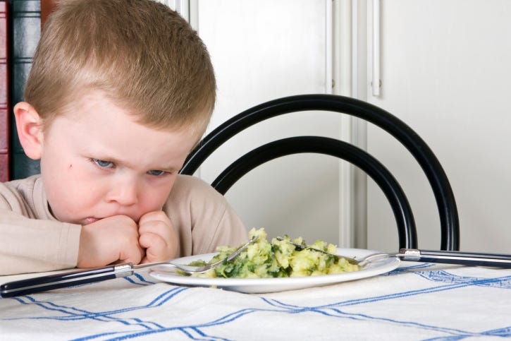 A child at the dinner table refusing to eat his vegetables
