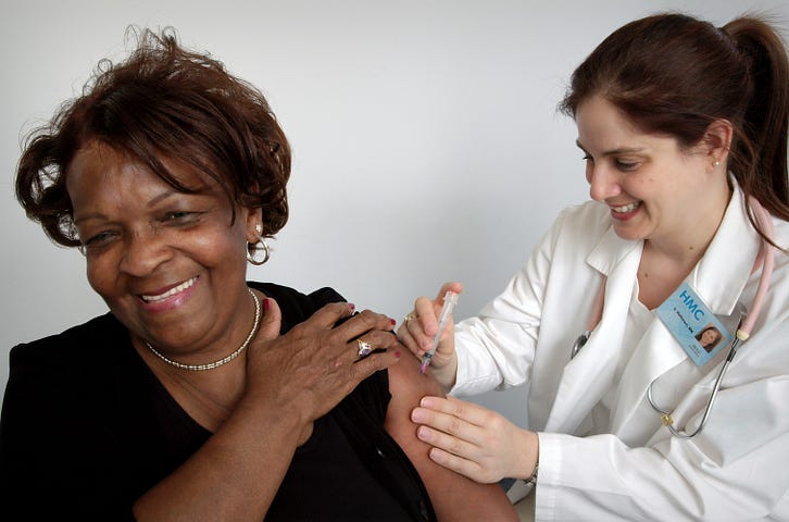 A patient smiles while a doctor administers a flu shot.