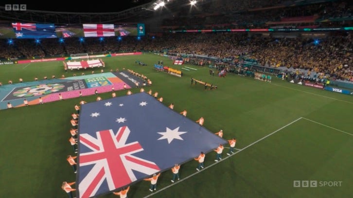 photo of stadium pitch with prominent Australian flag being held aloft