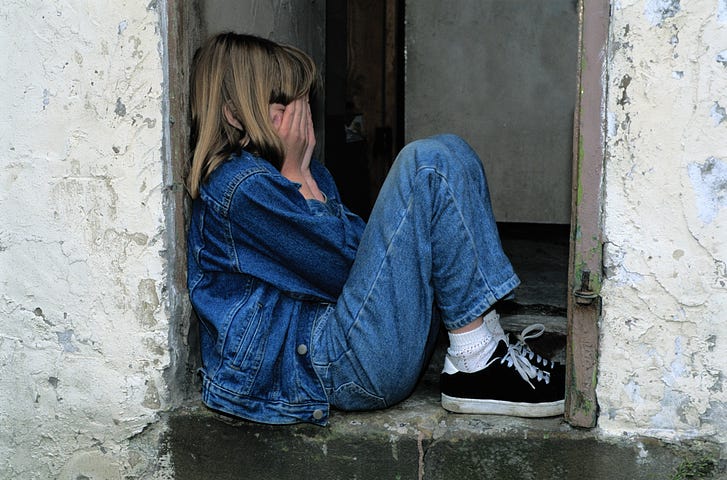 Sad young girl sitting in a doorway, crying with face in her hands.