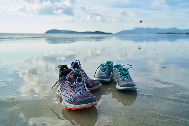 Two pairs of running shoes on a beach.