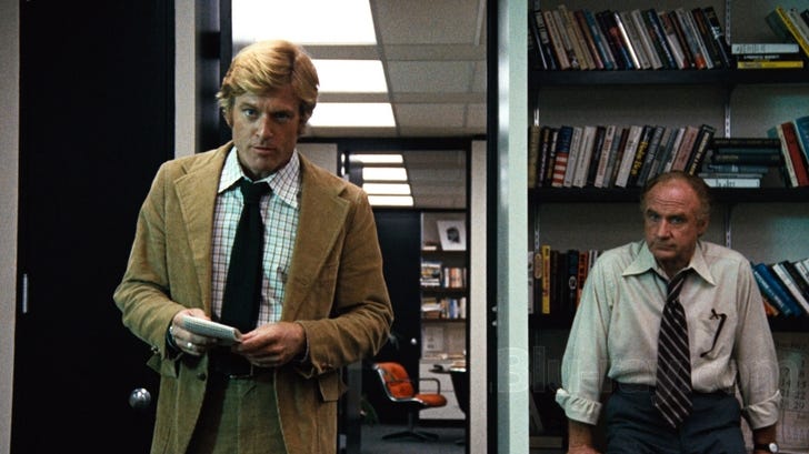 Still from the movie All the President’s Men. Robert Redford bursting into an office with a man standing next to him.
